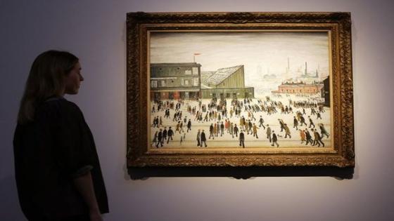 (FILES) In this file photo taken on September 29, 2022, a gallery assistant studies "Going to the Match" by English artist LS Lowry from 1953, in London, ahead of the Modern British & Irish Art Evening Sale. - The painting sold for £6.6m (7.57m Euros, 7.39m US Dollars) at auction in London on October 19, a record for a Lowry. (Photo by ISABEL INFANTES / AFP) / RESTRICTED TO EDITORIAL USE - MANDATORY MENTION OF THE ARTIST UPON PUBLICATION - TO ILLUSTRATE THE EVENT AS SPECIFIED IN THE CAPTION